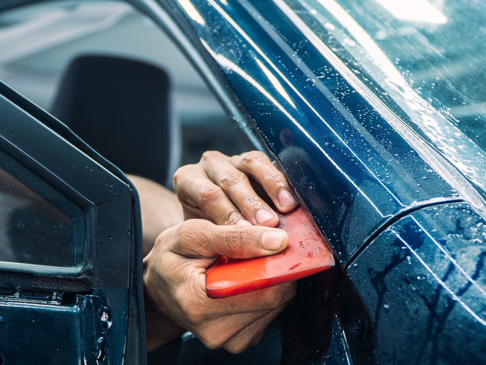 Installer squeegeeing paint protection film onto a wet deep-blue car panel